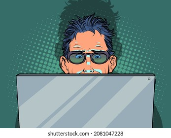 A man is looking at a laptop, the screen illuminates his face