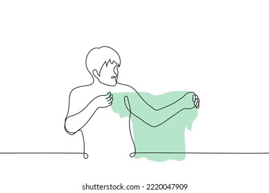 man looking at t-shirt - one line drawing vector. concept going to put on a t-shirt
