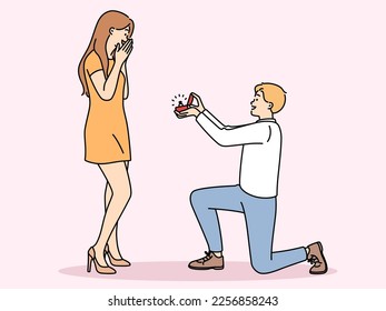 Man in love kneeling down, gives ring to beloved offering to marry and play wedding. Happy girl feels embarrassed covering mouth with hand after wedding proposals from boyfriend