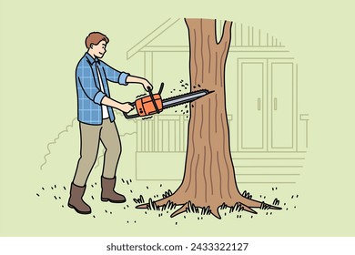 Man lumberjack uses chainsaw to get rid of old, diseased tree growing near house. Young guy works as lumberjack and helps residents of country cottages clear area of unnecessary trees.