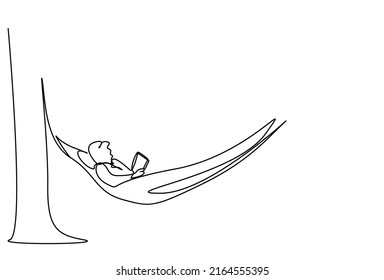 man lying in hammock on tree in garden on vacation reading a book calmly and focused