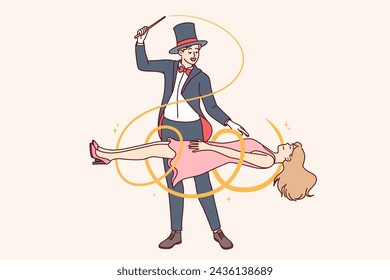 Man magician demonstrates magic trick by making woman assistant levitate during circus performance. Guy magician dressed in tuxedo and classic hat, entertaining audience with mysterious tricks