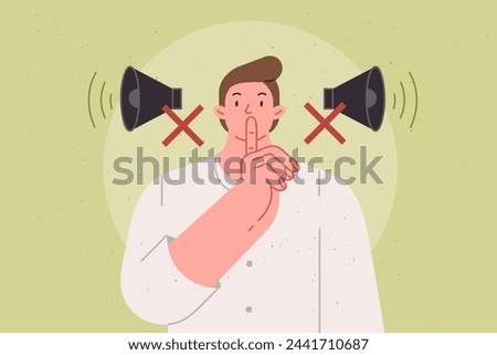 Man makes tss gesture urging to switch phone to airplane mode and speak in whisper, standing near crossed out megaphones. Guy recommends keeping quiet so as not to disturb people around him.