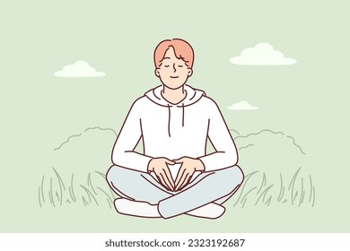 Man meditates sitting on green grass and practices yoga to restore strength and put thoughts in order. Peaceful guy meditates in meadow, wanting to achieve harmony or balance with nature.