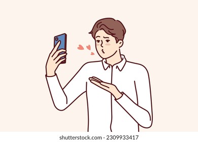 Man with mobile phone sends air kiss to interlocutor during video call to girlfriend who has left on business trip. Guy with smartphone records video of valentine wishing to kiss bride from distance