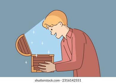 Man with open chest filled with treasures or jewels for concept of lucky find and luck. Delighted guy holds wooden chest with rays of light illuminating face and shouts WOW sees contents