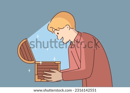 Man with open chest filled with treasures or jewels for concept of lucky find and luck. Delighted guy holds wooden chest with rays of light illuminating face and shouts WOW sees contents