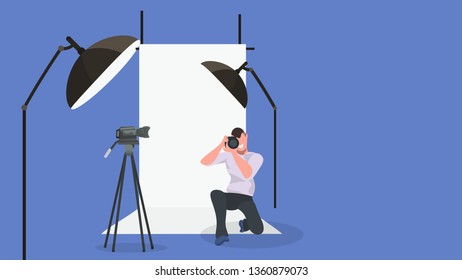 man photographer taking photo with camera male character standing on knee and shooting modern photo studio interior with lightning equipment horizontal full length