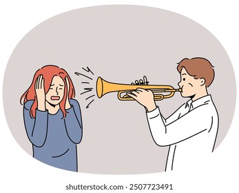 Man plays trumpet near woman covering ears, for concept trumpeter lack musical talent. Guy who wants to become professional musician learns to play compositions on trumpet and interferes with others