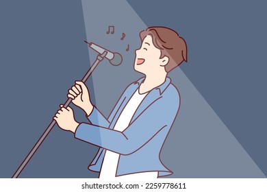 Man pop star sings song leaning back with microphone on tripod in hands during performance at concert. Happy guy performs popular song for own fans while standing in spotlight