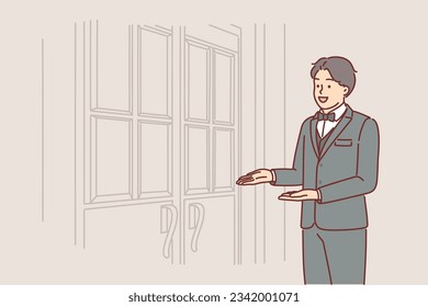 Man porter stands at door of restaurant inviting you to enter and saying welcome to guests of establishment. Guy doorman in expensive suit works at hotel meeting visitors near entrance