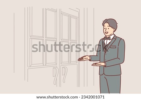 Man porter stands at door of restaurant inviting you to enter and saying welcome to guests of establishment. Guy doorman in expensive suit works at hotel meeting visitors near entrance