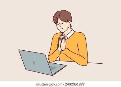 Man prays sitting in front of laptop and watching broadcast of religious event from catholic church. Praying young guy believes in god, prays before starting office work with computer.