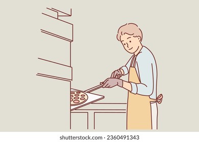 Man prepares pizza standing in kitchen Italian restaurant, working as chef and putting traditional thin-crust pie into oven. Guy in apron is making classic pizza with tomatoes and mozzarella cheese