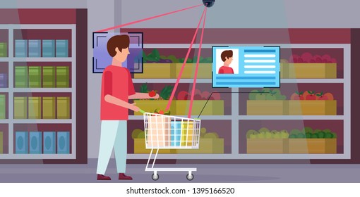 man pushing shopping trolley cart with groceries identification facial recognition concept security camera surveillance cctv system grocery shop supermarket interior full length horizontal