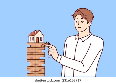 Man puts house in danger by pulling blocks from under building for concept of risky mortgage loan or pledge of real estate. House needs insurance and mortgage redemption from credit bank