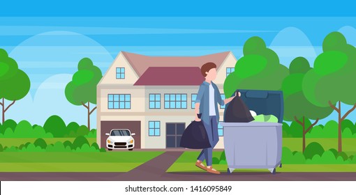 man putting two garbage bags in trash bin young guy doing housework cleaning service concept modern village house exterior full length flat landscape background horizontal