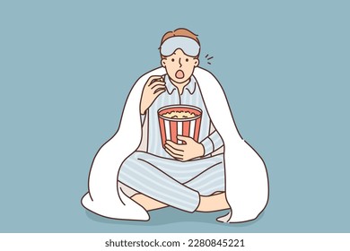 Un hombre en pijama bajo manta come una película de palomitas en casa. Un hombre sorprendido usa pijama y disfruta de una noche de cine en el interior con aperitivos. Ilustración vectorial. 