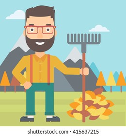 Man with rake standing near heap of autumn leaves.