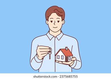 Man real estate broker holds keys and model house offering to take out mortgage on favorable terms. Real estate agent guy looks at screen and smiles, recommending to provide consultation services