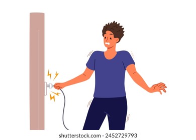 Man receives electric shock when inserts plug into socket and feels pain due to breakdown of electrical equipment. Electric shock for guy in casual clothes holding wire with wet hands