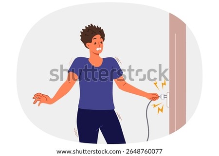 Man receives electric shock when inserts plug into socket and feels pain due to breakdown of electrical equipment. Electric shock for guy in casual clothes holding wire with wet hands