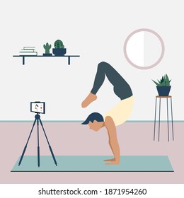 A man records a yoga video tutorial on his smartphone. A young man standing in the scorpion handstand pose Vrschikasana. Stay home concept. Home activity during quarantine. Online courses, education