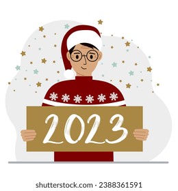 A man in a red sweater and with a cap holds a sign or poster with the numbers 2023. Postcard or greeting Merry Christmas and Happy New Year.