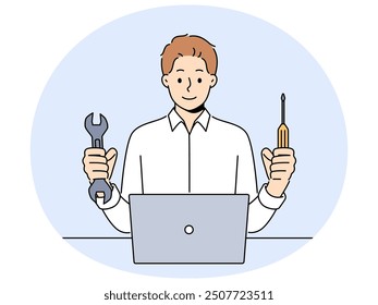 Man repairs laptop after breakdown and holds screwdriver and wrench in hands, working as system administrator. Guy fixes laptop or wants to upgrade by replacing hard drive of computer