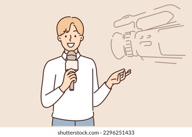 Man reporter with microphone stands near professional video camera filming TV documentary or entertainment show. Young guy working as reporter on television channel smiles and gesticulates