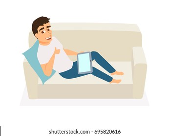 Man seating on couch, use tablet and show thumb. Guy communicates, orders food, gets education online or works at home on sofa. Freelancer at home. Leisure and relax.