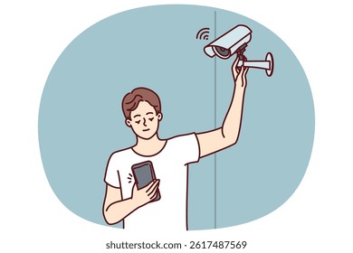 Man sets up WIFI camera and monitors result via phone to secure home. Young guy uses modern camera trusting video surveillance system and CCTV technology to protect apartment or business.