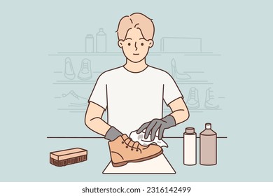 Man shoemaker cleans client leather boots after repair working in shoe shop. Young positive shoemaker guy uses professional shoe cosmetics to give boots shine and protect against leakage.