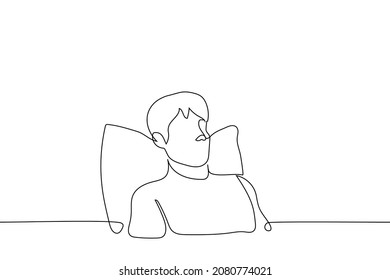 el hombre se sienta en la cama bajo su almohada de espalda - un vector de dibujo de una línea. concepto de estar en casa reclinándose en la cama 