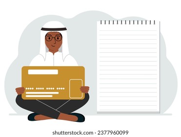 A man sits cross-legged in his hands holding a large credit card next to a close-up notepad for text. Concept of credit card, expense planning, income planning.
