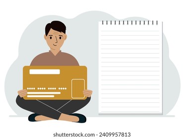 A man sits cross-legged in his hands holding a large credit card next to a close-up notepad for text. Concept of credit card, expense planning, income planning.