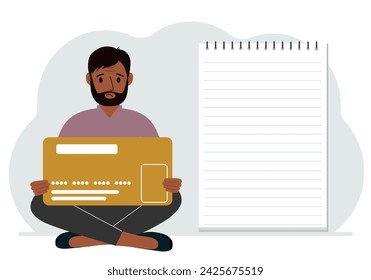 A man sits cross-legged in his hands holding a large credit card next to a close-up notepad for text. Concept of credit card, expense planning, income planning.