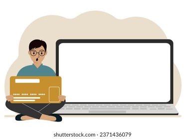 A man sits cross-legged and holds a large plastic card. Next to the man is a large laptop with space for text.