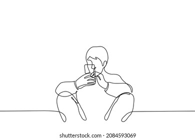 man sits leaning wall with back, apart and bent  knees holding phone with both hands - one line drawing vector