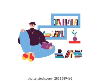 Man sits on the floor reading book next wall shelves, side table, and stacks of books on the floor.