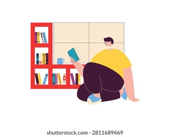 Man sits on the floor reading a book in front of a low, multi-compartment bookcase.