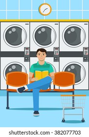 A man sits on a plastic seat, reading a book and waiting for the end of washing clothes in launderette