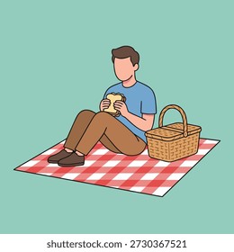 A man sits on a red and white checkered blanket, eating a sandwich next to a picnic basket, enjoying a meal outdoors.