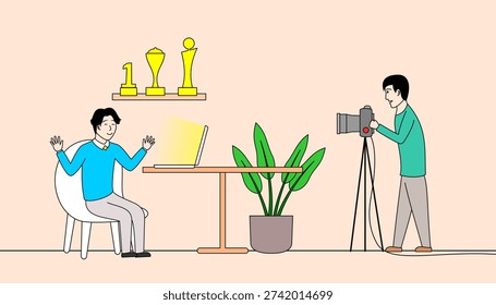 Man sits at a table with a laptop, while another man takes a picture with a camera. The scene is set in a room with a potted plant and a shelf with trophies. Scene is focused and professional