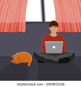 A man sitting cross legged using computer in front of the window with his sleeping cat