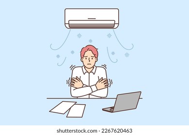 Man sitting at office desk under air conditioner freezes due to cold temperatures or broken climate equipment. Guy tries to warm up after being cold during working day