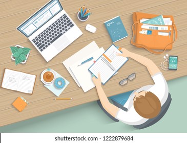 Man sitting at the wooden table. Workplace Desktop Workspace Armchair, office supplies, monitor, books, notebook, headphones, phone, glasses, pen, bag, tea, donut. Vector Top view 