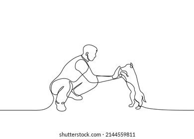 man squatting greets a dog - one line drawing vector. the concept of friendship and love between a man and a dog, a dog lover gives five to a dog, training