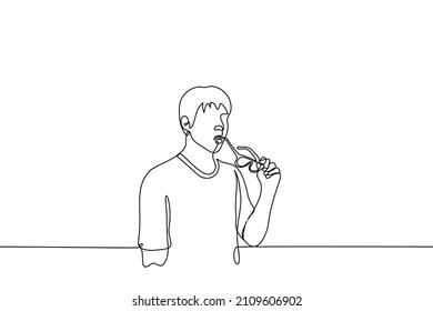 man standing biting frame of his glasses - one line drawing vector. man surprised, fascinated or thoughtful