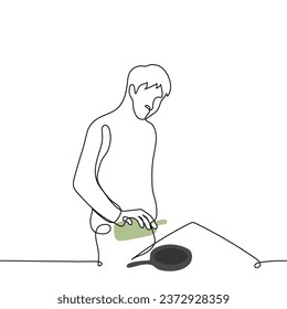 man standing in front of the stove pouring olive oil from a bottle into a frying pan - one line art vector. concept to cook healthy food at home